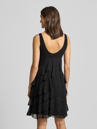 Frauenmodel trägt Knielanges Cocktailkleid mit Volants von Swing aus schwarzem Chiffon, A-Linie, Knielänge, Rückenansicht, Ganzkörperansicht Rückansicht. Rückenlänge bei Größe 36: 103 cm, Brustweite bei Größe 36: 31 cm, Rundhalsausschnitt, Volants.