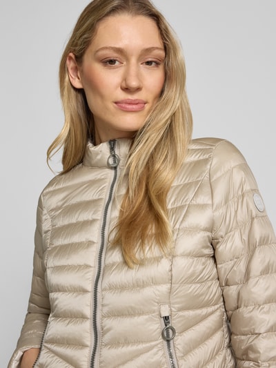 Frauenmodel trägt Steppjacke mit Stehkragen von Gil Bret in Beige, körpernahe Passform, Zweiwege-Reißverschluss, Reißverschlusstaschen, Nahaufnahme Oberkörper. Rückenlänge 56 cm, Schulterbreite 39 cm, Brustweite 47 cm, Ärmellänge 66 cm, Größe 36.