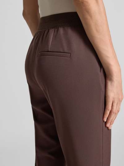 Frauenmodel trägt Regular Fit Anzughose mit elastischem Bund von s.Oliver BLACK LABEL in Dunkelbraun, Struktur sichtbar, Nahaufnahme Rückansicht.