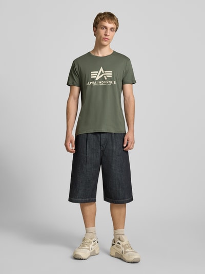 Mannenmodel draagt T-shirt met logo en ronde hals van Alpha Industries, puur katoen, regular fit, ruglengte maat M 68 cm, geheel vooraanzicht.