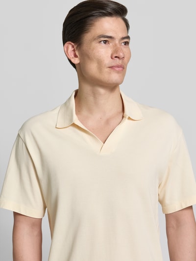Męski model nosi Relaxed Fit Poloshirt in Pique-Optik od Scotch & Soda z czystej bawełny, kremowy kolor, krótki rękaw, krój relaxed fit, piqué, polokołnierzyk, długość tyłu w rozmiarze M: 70 cm, zbliżenie na górną część ciała.