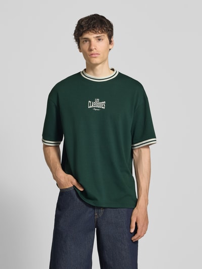 Männermodel trägt Boxy Fit T-Shirt aus reiner Baumwolle Modell 'LES' von Only & Sons in Optik: Unifarben mit Label-Print, Ganzkörperansicht von vorne.