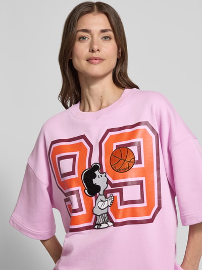 Frauenmodel trägt Loose Fit Sweatshirt mit Snoopy®-Print Modell 'JUMPI EMBO' von Essentiel Antwerp in Rosa, Motiv-Applikation vorne, Nahaufnahme Oberkörper.