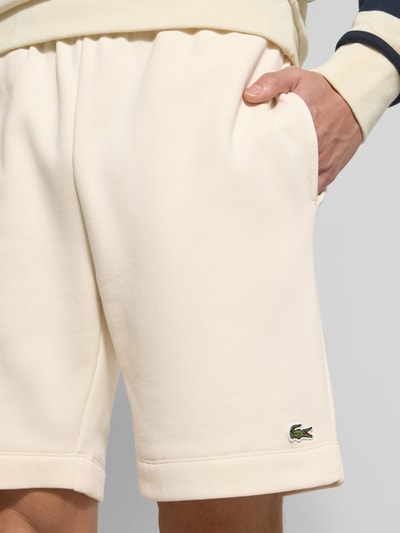 Mannenmodel draagt Regular Fit Sweatshorts aus Baumwoll-Mix van Lacoste in effen kleuren met labelpatch, katoenmix sweat, steekzakken, achterzak, verstelbare wijdte met tunnelkoord, detailopname bovenbeen.