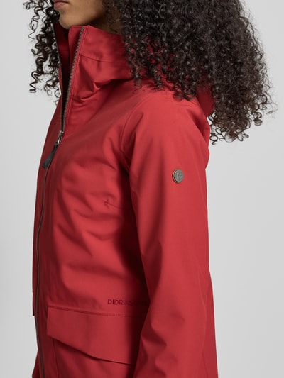 Frauenmodel trägt Regular Fit Parka mit Logo-Applikation Modell 'Folka' von Didriksons, rot, Stehkragen mit Kapuze, Detailaufnahme Oberkörper.