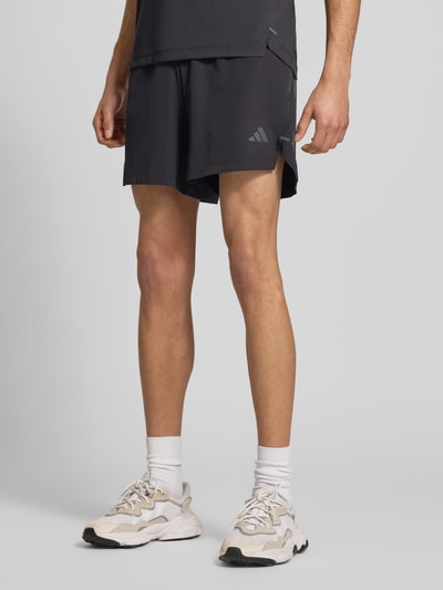 Männermodel trägt Regular Fit Sport-Shorts mit Logo-Print von adidas Training, Optik: Unifarben, Ganzkörperansicht von vorne.