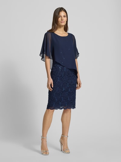 Frauenmodel trägt Knielanges Cocktailkleid mit Paillettenbesatz von SWING, dopasowany krój, długość do kolan, okrągły dekolt, efekt podpalania, długość tyłu 95 cm, szerokość klatki piersiowej 36 cm, granatowy kolor, tekstura cekinowego obszycia, całkowita długość, widok z przodu, całopostaciowa perspektywa.