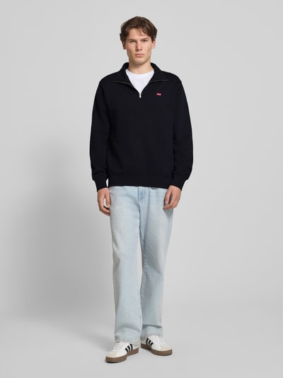Männermodel trägt Regular Fit Sweatshirt aus reiner Baumwolle von Levi's®, dunkelblau, weiße Jeans, Ganzkörperansicht von vorne.