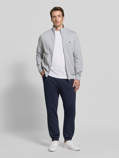 Männermodel trägt eine graue Regular Fit Sweatjacke aus Baumwoll-Mix von Lacoste, glatte Oberfläche, Ganzkörperansicht von vorne. Herren Sweatjacke von Lacoste.