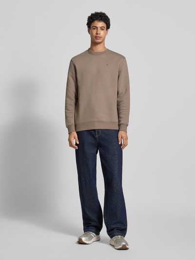 Męski model nosi Regular Fit Sweatshirt aus Baumwoll-Mix od Tommy Jeans, efekt: jednolity kolor, krój regular fit, wyhaftowane logo, okrągły dekolt, długi rękaw, zakończenie rękawów i dół prążkowane, dzianina dresowa, mieszanka bawełny; pełny widok z przodu.