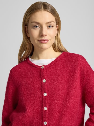 Vrouwenmodel draagt Cardigan aus Woll-Mix mit Rundhalsausschnitt Modell 'VITOW' van American Vintage, regular fit, rode kleur, knoopsluiting, mix met alpaca, detailopname bovenlichaam.