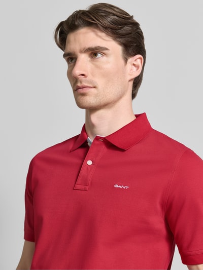 Männermodel trägt Regular Fit Poloshirt mit Logo-Stitching von Gant in Rot, elastischer Baumwoll-Mix, Nahaufnahme Oberkörper.