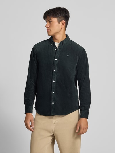 Männermodel trägt Regular Fit Freizeithemd mit Logo-Stitching Modell 'MADISON' von Carhartt Work In Progress, Nahaufnahme Oberkörper. Reine Baumwolle, dunkelgrüne Farbe, sichtbare Knopfleiste und Button-Down-Kragen, dezente Struktur.