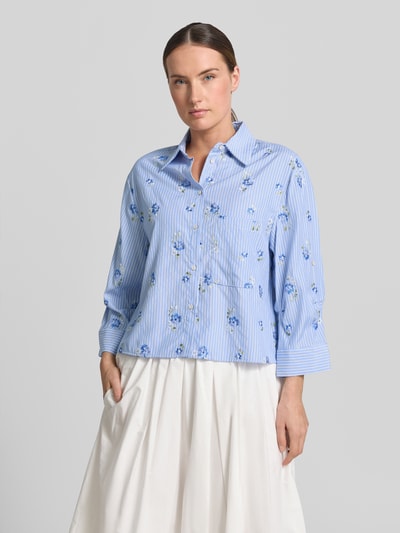 Frauenmodel trägt Hemdbluse mit Knopfleiste Modell 'FLORIX' von Mango, blau mit Blumen-Muster, Material-Mix mit Viskose-Anteil, Regular-Fit, Hemdblusenkragen, Rückenlänge 49 cm, Ärmellänge 46 cm, Ganzkörperansicht von vorne.