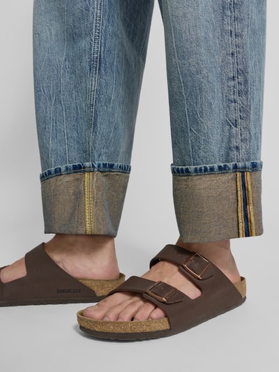 Mężczyzna nosi jeansy model 'RAWDY' od DRYKORN, bawełna, krój relaxed fit, efekt znoszenia, brzeg, zdjęcie zbliżenie dolnej części nóg. Szerokość w rozmiarze 32/32: 46 cm, długość wewnętrzna nogawki: 68 cm.