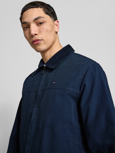 Männermodel trägt Regular Fit Blouson aus reiner Baumwolle von Tommy Jeans in Dunkelblau, Logo-Stitching, Nahaufnahme Oberkörper.