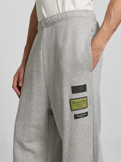 Männermodel trägt Wide Fit Sweatpants mit Logo-Patch von MM6 Maison Margiela in Hellgrau, reine Baumwolle, Nahaufnahme Oberschenkel.