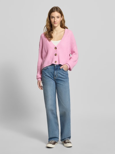 Frauenmodel trägt Regular Fit Strickjacke mit einreihiger Knopfleiste Modell 'CAROL NICE' von Only in Rosa, unifarben, Strickoptik, ganzkörperansicht von vorne.
