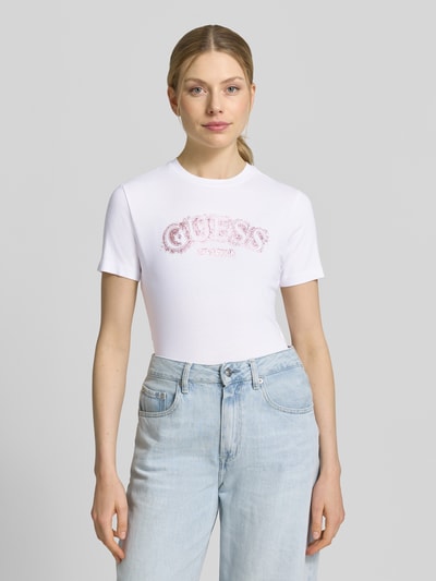 Vrouwenmodel draagt T-Shirt uit Viskose-Elasthan-mix met logo van Guess Activewear, regular fit, ronde hals, witte kleur, voorkantopname, ruglengte maat S 53 cm.