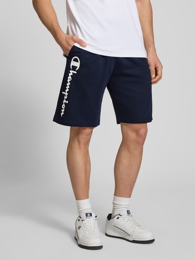 Männermodel trägt Shorts mit Logo-Print und -Stitching von CHAMPION in Dunkelblau, Baumwoll-Mix, lockerer Schnitt, Ganzkörperansicht von vorne