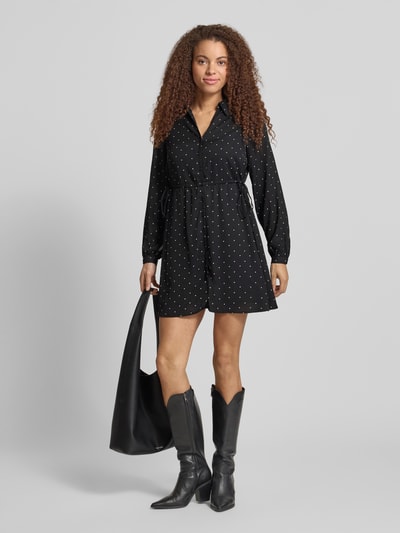 Modelka nosi Tailliertes Freizeitkleid mit Allover-Muster Modell 'ALYNN' od Only, efekt: wzór na całej powierzchni, krój: taliowany, długość: mini, dekolt: wysokie zapięcie, ściągacz w talii, listwa guzikowa, długi rękaw z mankietem, widoczne czarne kolory i delikatny wzór, tekstura gładka, Ganzkörperansicht von vorne.