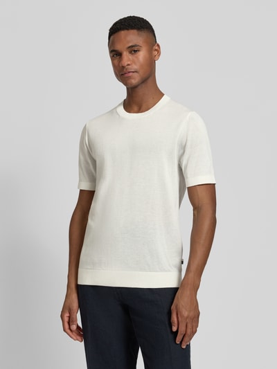 Męski model nosi Strickshirt mit Rundhalsausschnitt und 1/2-Arm von OLYMP Level Five, mieszanka bawełny i lyocellu, krój regular fit, okrągły dekolt, rękaw o dł. 1/2, długość tyłu w rozmiarze M: 67 cm, jasny kolor, gładka faktura, widok całej sylwetki z przodu.
