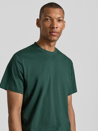 Męski model nosi Relaxed Fit T-Shirt aus reiner Baumwolle Modell 'ASPEN' von SELECTED HOMME, ciemnozielony, gładki, zbliżenie na górną część ciała.