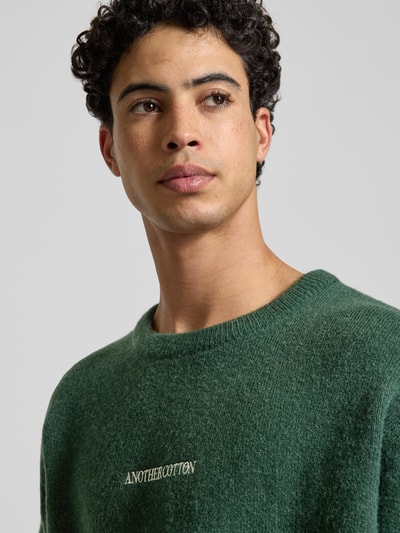 Männermodel trägt Strickpullover mit gerippten Abschlüssen von ANOTHER COTTON LAB, Material-Mix, Rundhalsausschnitt, Label-Stitching, Nahaufnahme Oberkörper.