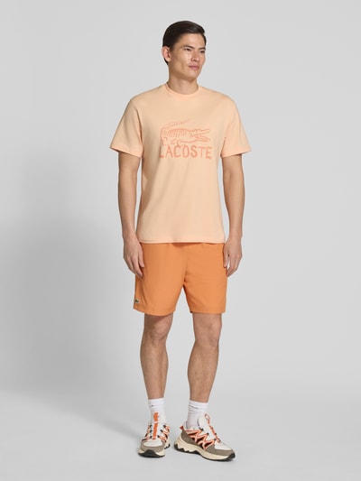Mannenmodel draagt Regular Fit T-shirt aus reiner Baumwolle van Lacoste in look: effen, logoprint, korte mouw, ronde hals, puur katoen. Ganzkörperansicht van voren.