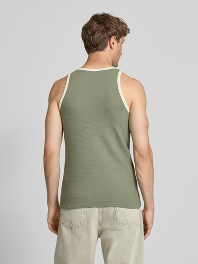 Męski model nosi Slim Fit Top mit Logo-Stitching von KARL KANI, bawełna, krój slim fit, wzór strukturalny, oliwkowy, widok całej sylwetki z tyłu.