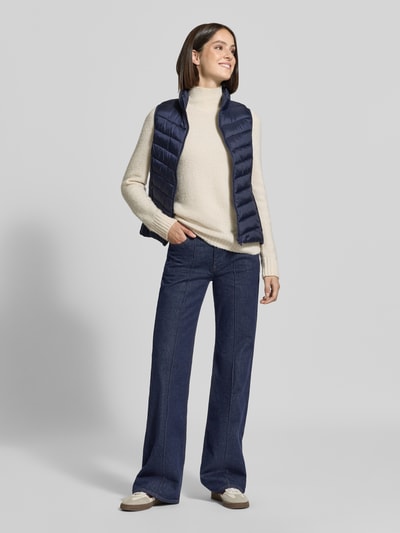 Modelka kobieca nosi granatową kamizelkę Regular Fit Weste mit Stehkragen von Jake*s Casual, połączoną z jasnym swetrem, ciemnoniebieskimi spodniami i jasnymi butami, całkowity widok z przodu.