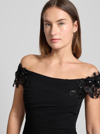 Vrouwenmodel draagt Abendkleid im Off-Shoulder-Look van Lipsy, zwart, getailleerd, stretchmateriaal, detail op schouders, Nahaufnahme bovenlichaam.