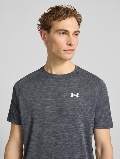 Männermodel trägt T-Shirt mit Label-Print Modell 'Tech' von Under Armour in Grau, Herren T-Shirt im Gerader-Schnitt, Nahaufnahme Oberkörper. Rückenlänge bei Größe M: 75 cm, Rundhalsausschnitt, Tech-Material.