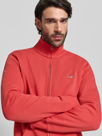 Męski model nosi Regular Fit Sweatjacke mit Stehkragen Modell 'Gield' od Gant, kolor koralowy, logo, bawełniany miks, zamek, widok na górną część ciała z przodu.
