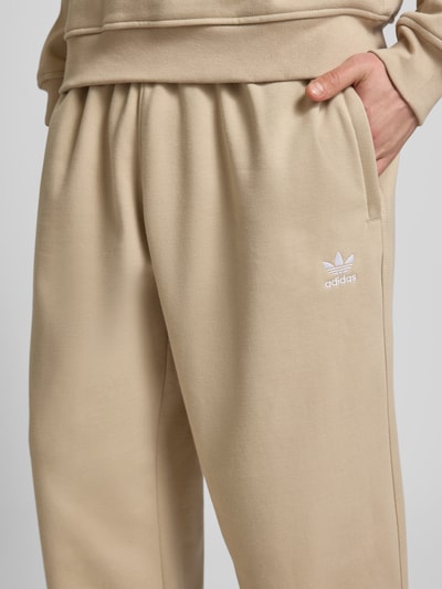 Mężczyzna nosi Wide Fit Sweatpants mit elastischem Bund od adidas Originals, bawełniana mieszanka, logo, zbliżenie na biodra