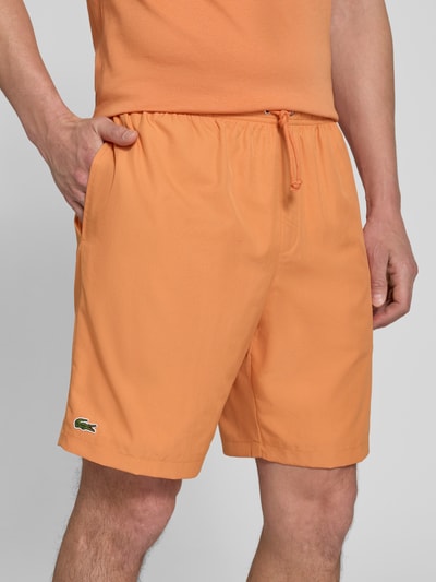 Männermodel draagt Relaxed Fit Sport-Shorts met logo-stitching van Lacoste, look: effen kleuren, pasvorm: relaxed fit, applicatie: gestikt logo, sluiting: tunnelkoord, boord: elastisch, zij-steekzakken, detailopname bovenbenen.