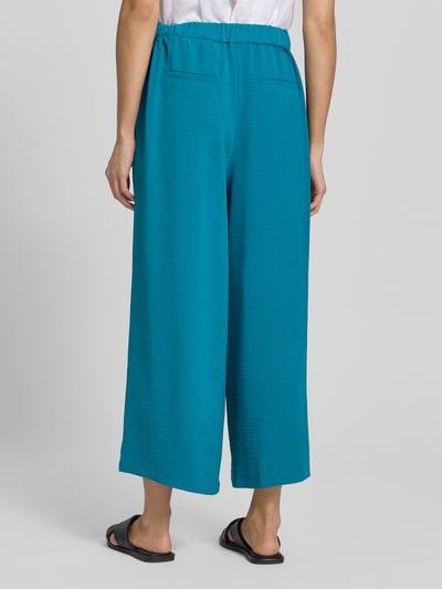 Frauenmodel trägt Culotte mit französischen Eingrifftaschen von zero, loose Fit, elastischer Bund, Gürtel, leuchtend türkis, angedeutete Gesäßleistentaschen, strukturierte Oberfläche, Ganzkörperansicht Rückansicht.