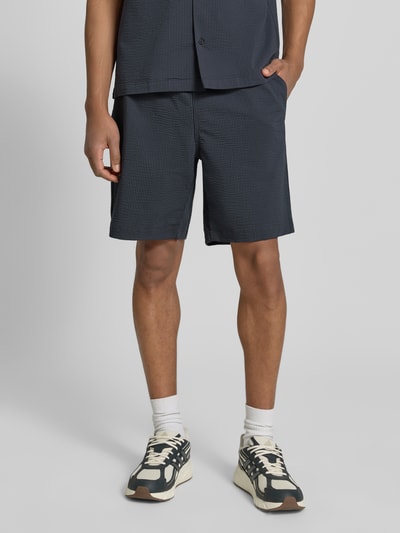 Männermodel trägt Loose Fit Shorts aus Baumwoll-Mix von Lacoste, Optik:Allover-Muster, gestreift, Materialverarbeitung: Seersucker, Ganzkörperansicht von vorne.