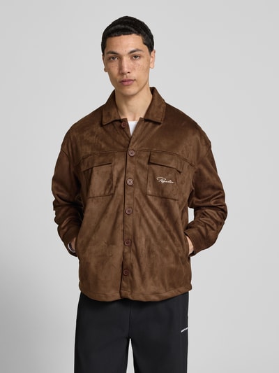 Męski model nosi Relaxed Fit Hemdjacke mit Brusttaschen Modell 'Madikeri' od Pegador, brązowa skórzana tekstura, kieszenie na piersi, guzik, Kent kołnierz, haft z logo, widok całej sylwetki z przodu.