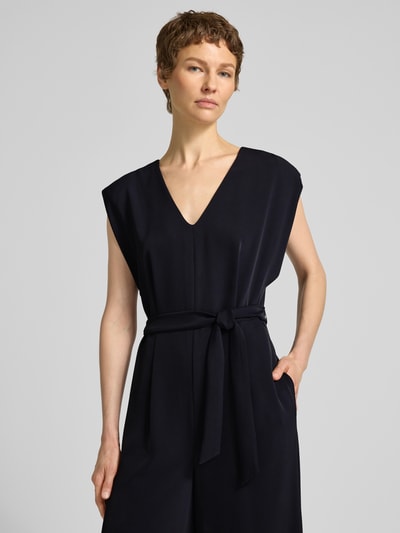 Frauenmodel trägt Jumpsuit mit V-Ausschnitt und Bindegürtel von comma, dunkelblauer Material-Mix mit Stretch, Regular Fit, Nahaufnahme Oberkörper.