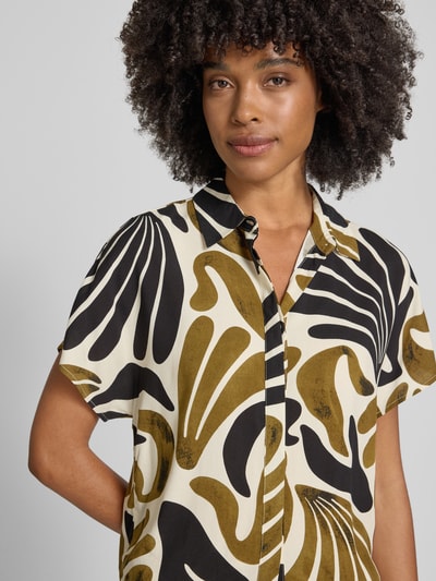 Frauenmodel trägt Regular Fit Bluse aus Viskose mit Knotendetail Modell 'FELDI' von Soyaconcept im Allover-Look mit Hemdblusenkragen, verdeckter Knopfleiste, kurzer Ärmellänge, Rückenlänge 54 cm, Farbmix aus Schwarz, Weiß und Oliv, fließende Textur, Nahaufnahme Oberkörper.
