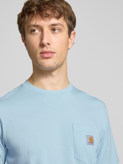 Männermodel trägt Regular Fit T-Shirt mit Logo-Patch von Carhartt Work In Progress in Hellblau, reine Baumwolle, Brusttasche, Nahaufnahme Oberkörper.