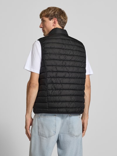 Männermodel trägt Steppweste mit Reißverschlusstaschen Modell 'ELVIS' von JACK & JONES in Schwarz, Ganzkörperansicht Rückansicht. Regular Fit, Stehkragen, sichtbare Steppnähte, glatte Textur, Rückenlänge bei Größe M 67 cm, Schulterbreite 41 cm, Brustweite 54 cm, Label-Detail.