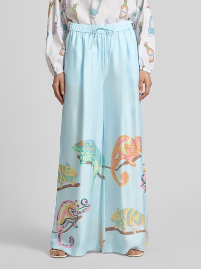 Frauenmodel trägt Wide Fit Seidenhose mit Motiv-Print von HERZENS in Hellblau mit elastischem Bund, Eingrifftaschen, Motiv-Print; Nahaufnahme Vorderansicht.
