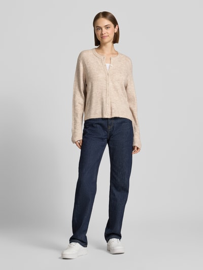 Frauenmodel trägt Loose Fit Strickjacke mit Rundhalsausschnitt Modell 'SIMONI' von ONLY in Beige zu Jeans, Damen Strickjacke, Ganzkörperansicht von vorne.