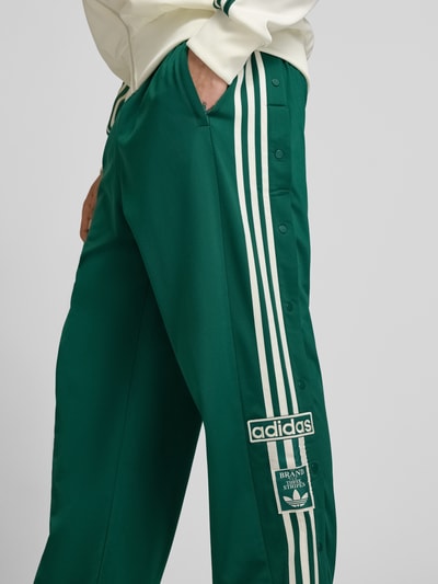 Männermodel trägt Sweatpants mit elastischem Bund Modell "ADIBREAK" von adidas Originals, grün mit weißen Streifen, Eingrifftaschen, Label-Stitching, Lockerer-Schnitt, Innenbeinlänge bei Größe M: 74 cm, Nahaufnahme Oberschenkel.