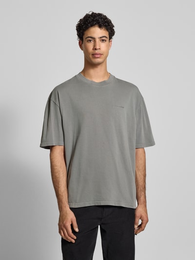 Männermodel trägt Oversized T-Shirt mit Label-Stitching von Pegador in Grau, reine Baumwolle, gerippter Rundhalsausschnitt, Ganzkörperansicht von vorne.