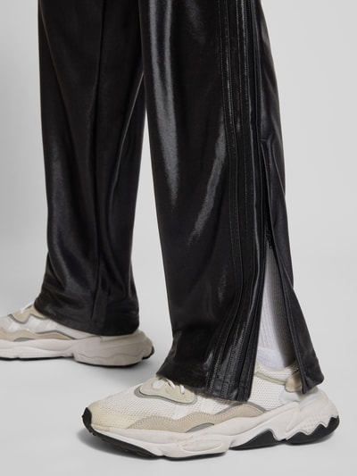 Mężczyzna nosi spodnie treningowe z logo model 'FIREBIRD' od adidas Originals, krój regular fit, czarne, elastyczny pas, długość wewnętrzna nogawki 79 cm dla rozmiaru M, detal nogawki, zbliżenie na dolną część nogawki