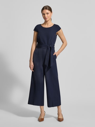 Kobiece modelka nosi Kombinezon mit Bindegürtel od Christian Berg Woman Selection, mieszanka materiałów z dodatkiem streczu, krój regular fit, okrągły dekolt, wiązany pasek, długość tyłu w rozmiarze 36: 39 cm, szerokość w rozmiarze 36: 37 cm, długość rękawów w rozmiarze 36: 7 cm, całkowita długość w rozmiarze 36: 130 cm, długość wewnętrzna nogawki w rozmiarze 36: 61 cm, ciemnoniebieski, gładka tekstura, szerokie nogawki, pełny widok z przodu