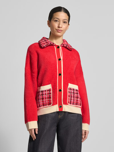 Vrouwenmodel draagt Boxy Fit Strickjacke met Ripp-Bündchen Modell 'JOILU' van Essentiel Antwerp in color blocking, contrasterende details, geribde zoom en manchetten, opgestikte steekzakken, geruite overhemdkraag, eenrijige knoopsluiting, gebreide structuur, kleur rood en beige. Vooraanzicht bovenlichaam.